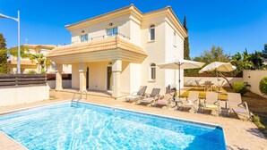 A poolside area with a clear blue pool, lounge chairs, and a building with a tiled roof. - Villa Livia in Paralimni (Paralimni)