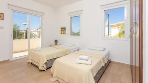 A hotel room with two beds, a sliding glass door to the outside, and a small table with a lamp. - Villa Livia in Paralimni (Paralimni)