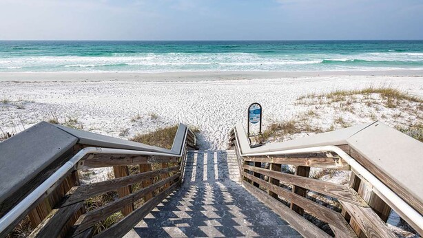 Ein hölzerner Steg führt zu einem Strand mit freiem Blick auf das Meer.