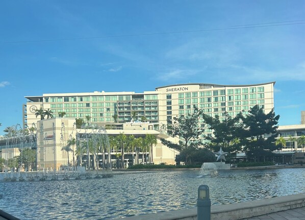 Un hotel Sheraton con una gran fuente de agua al frente, rodeado de palmeras y un cielo azul despejado.