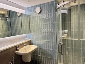 A modern bathroom with a large mirror, a sink, and a glass-enclosed shower.