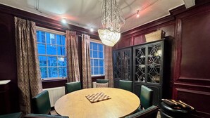 Une table ronde en bois, surmontée d’un échiquier, entourée de chaises recouvertes d’un tissu vert.