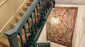 Un escalier avec une main courante en bois foncé et des marches recouvertes d’une moquette beige, décoré d’une guirlande de verdure et de baies rouges.