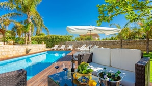Ein Poolbereich mit Korbsessel, Liegestühlen, einem Tisch mit Getränken und Blick auf den Pool.