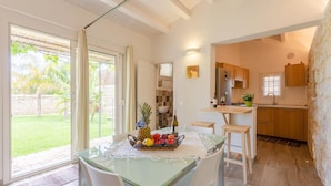 Eine helle Küche mit Essbereich, mit einem Tisch mit Früchten und einer Flasche, Holzschränken und Blick auf den Garten.