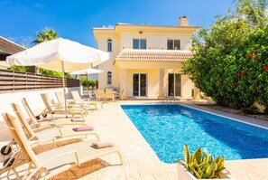 A swimming pool with lounge chairs and umbrellas, a building with a tiled roof, and a well-maintained garden. - Villa Clara in Paralimni (Paralimni)