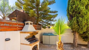 Un área de barbacoa con horno de piedra, una estructura de madera y un cobertizo.
