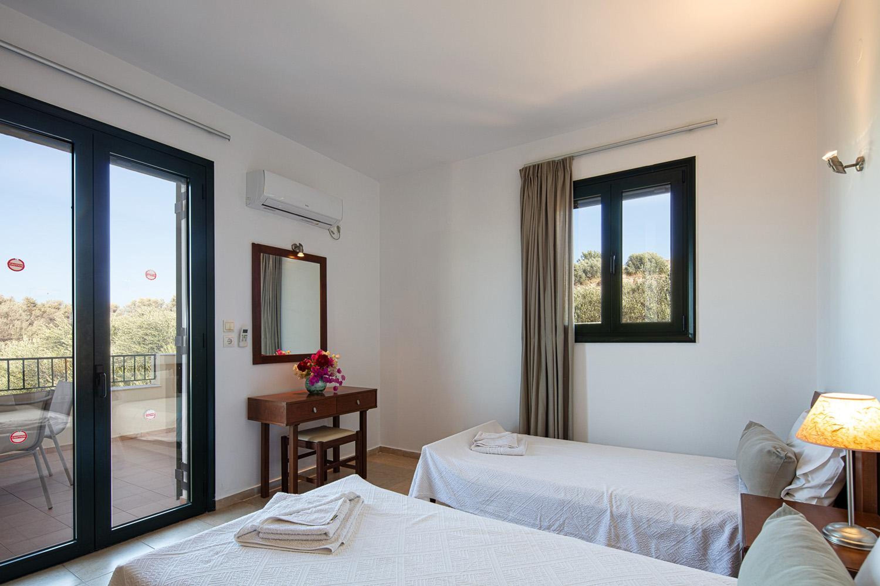 Une chambre d’hôtel avec deux lits, un bureau avec une chaise, une fenêtre avec des rideaux et un appareil de climatisation.