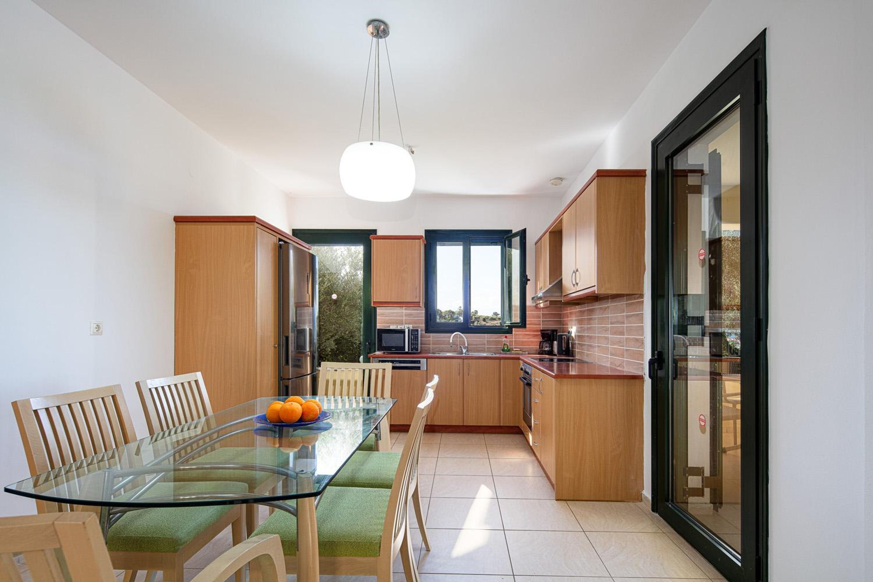 Une cuisine moderne avec une table à manger en verre, des chaises en bois et une vue sur l’extérieur.