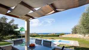 A covered outdoor area with a pool, a table with chairs, and a view of the sea. - Villa Eleni in Pigianos Kampos (Rethymno)