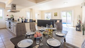 A spacious dining area with a central island, a kitchen in the background, and a large window providing natural light. - Villa Claudia in Paralimni (Paralimni)