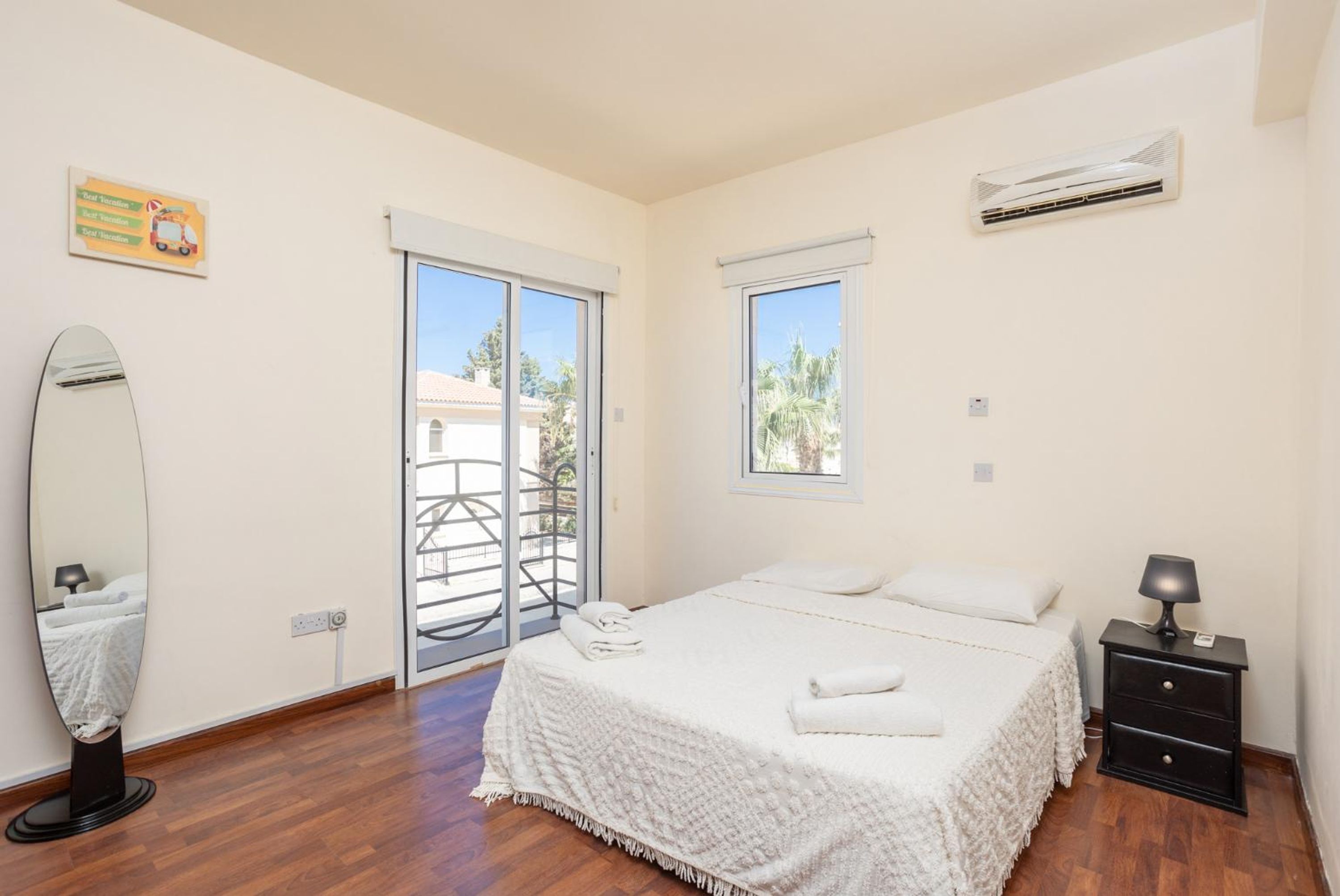 A bedroom with a bed, a nightstand, a mirror, and a sliding glass door leading to a balcony.
