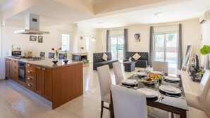 A modern kitchen with a central island, dining area with a table set for four, and a living area with a sofa and chairs. - Villa Koula in Paralimni (Paralimni)