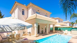 A poolside area with lounge chairs, a covered seating area, and a clear blue pool. - Villa Koula in Paralimni (Paralimni)