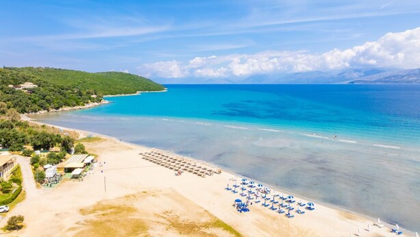Ein Strand mit klarem türkisblauem Wasser, einem sandigen Ufer und einer Reihe blauer Sonnenschirme.