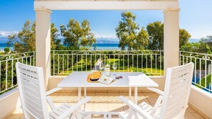 Ein Balkon mit Tisch für zwei Personen, mit Blick auf eine malerische Landschaft aus Meer und Grün.