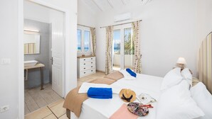 Ein Schlafzimmer mit Bett, Nachttisch, Fenster und einem Badezimmer mit Waschbecken und Spiegel.
