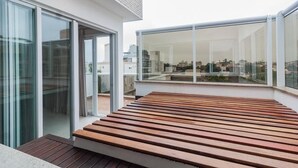 Eine moderne Dachterrasse mit Holzboden, großen Schiebeglastüren und weitläufigen Fenstern mit Blick auf die Stadt.