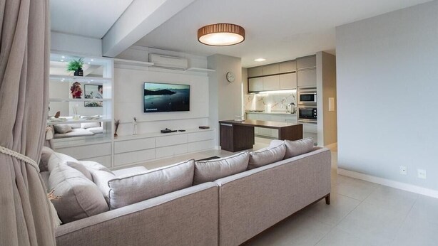 Ein modernes Wohnzimmer mit einer großen Couch, einem Flachbildfernseher und einer Küchenzeile mit integrierten Geräten.