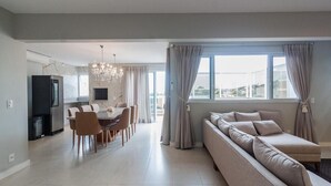 Ein modernes Wohnzimmer mit einer Couch, einem Essbereich mit Stühlen, einem Fernseher und einer Pendelleuchte.