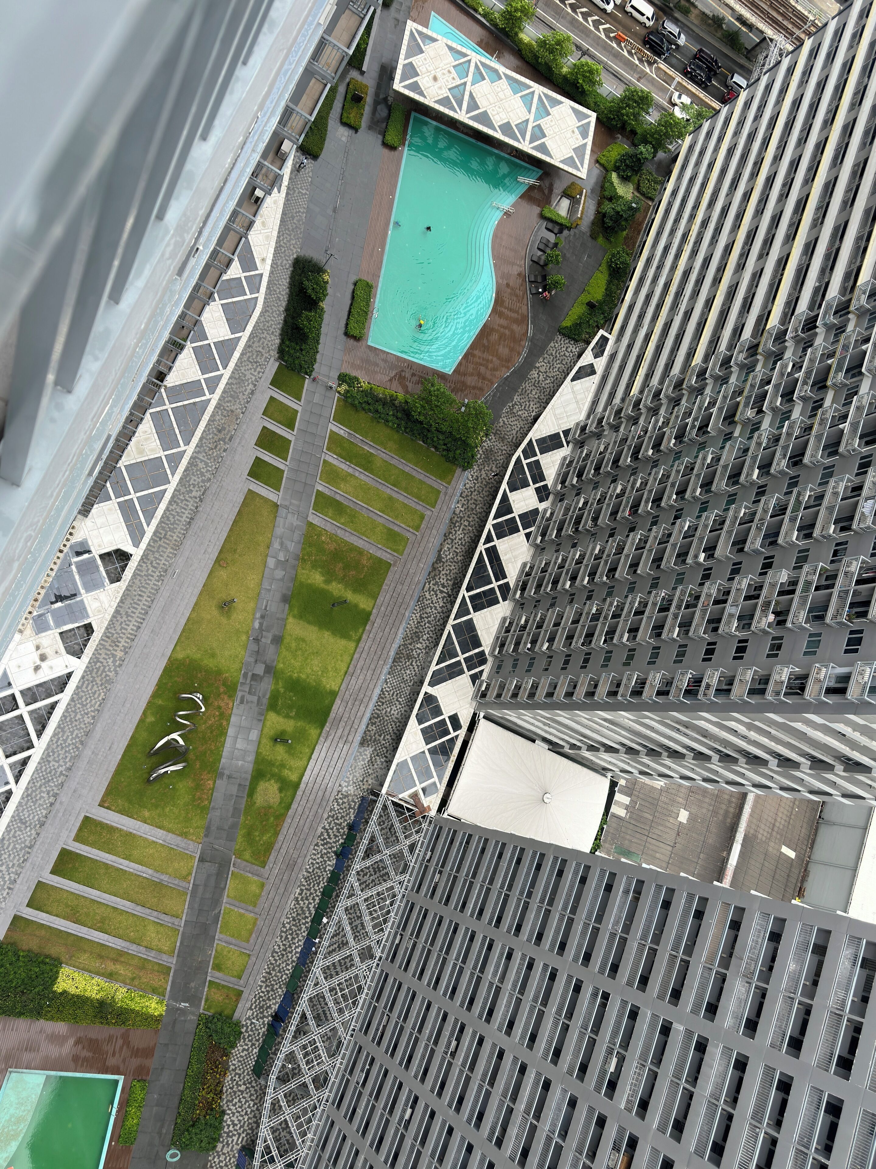 A high-rise building with a rooftop pool, a landscaped area with pathways, and a parking lot.