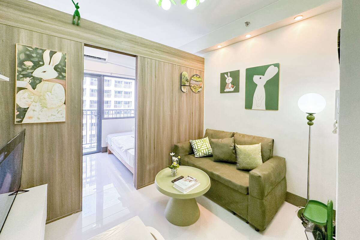 Une chambre d’hôtel moderne avec un canapé vert, une table basse ronde et des œuvres d’art représentant des lapins.