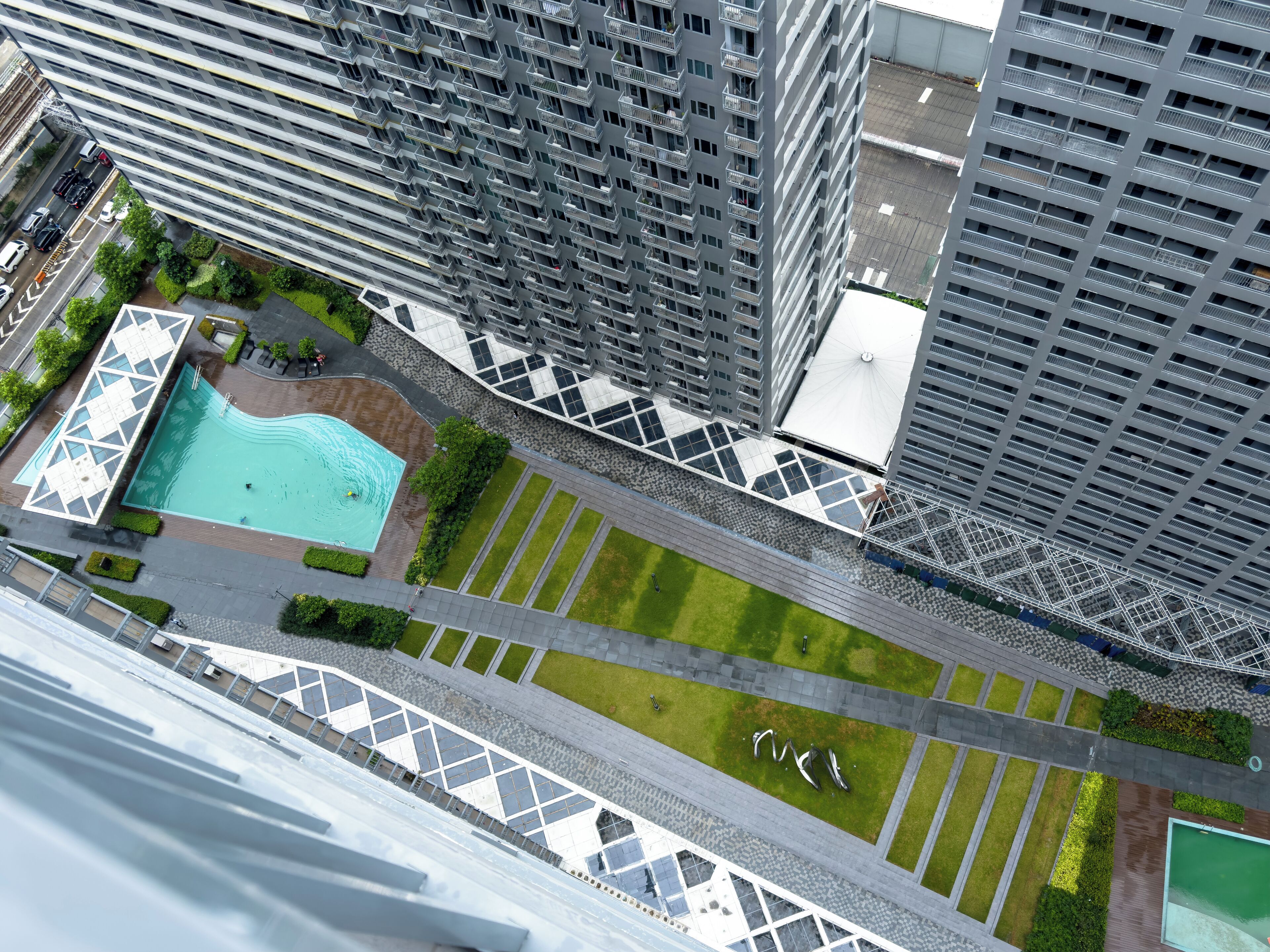 A high-rise building with a rooftop pool, green spaces, and a pedestrian walkway.