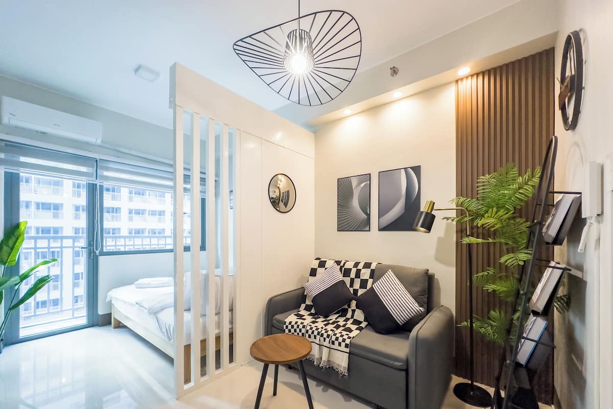 Un salon moderne avec un canapé gris, un plaid à carreaux noir et blanc, une petite table d’appoint en bois et une grande plante en pot.