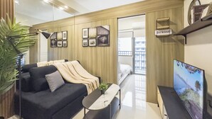 Un soggiorno moderno con divano, tavolino e televisore. Si nota una pianta, quadri appesi al muro e una finestra con vista sugli edifici.