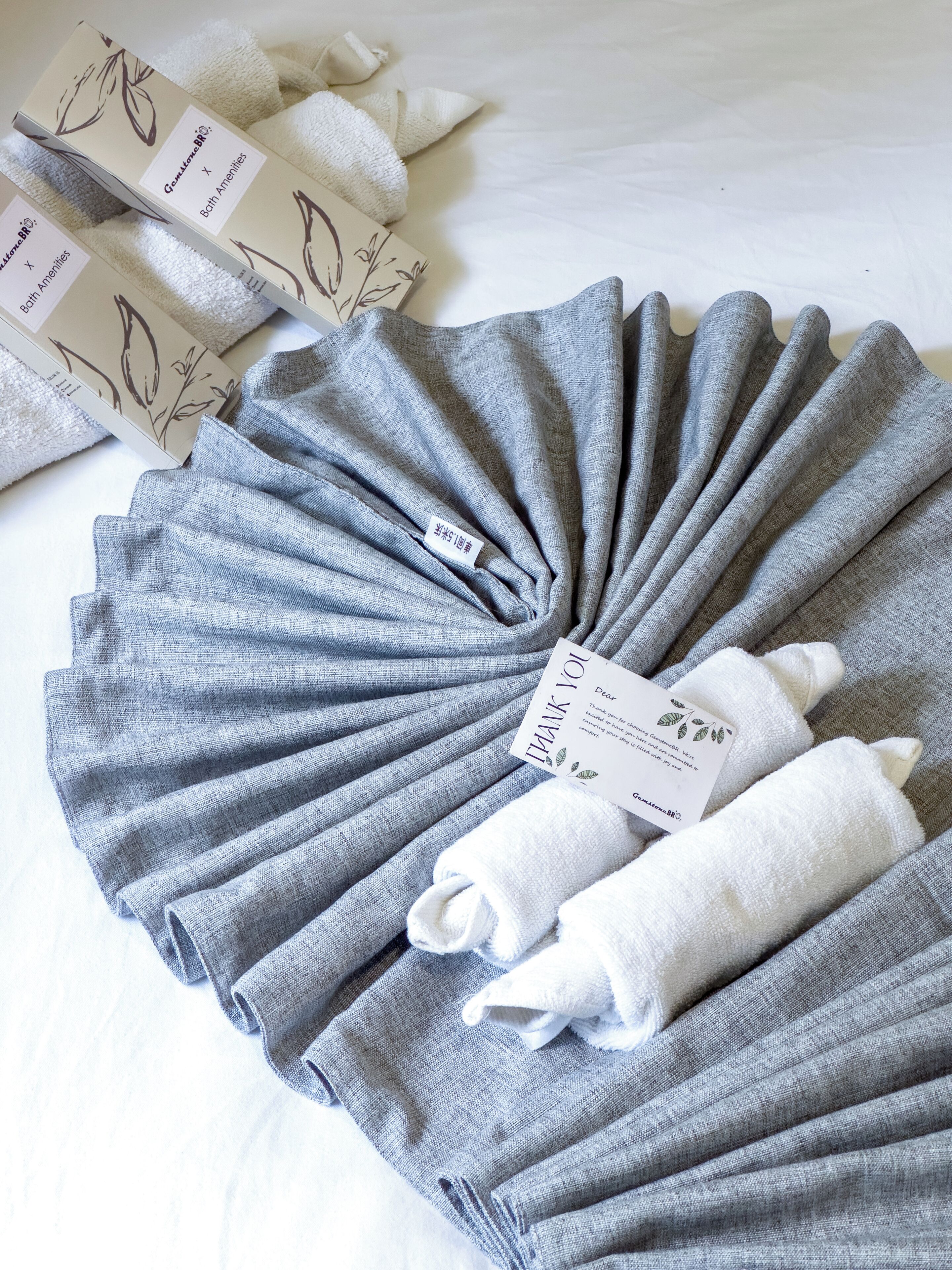 A neatly arranged set of towels and a thank you card on a bed.