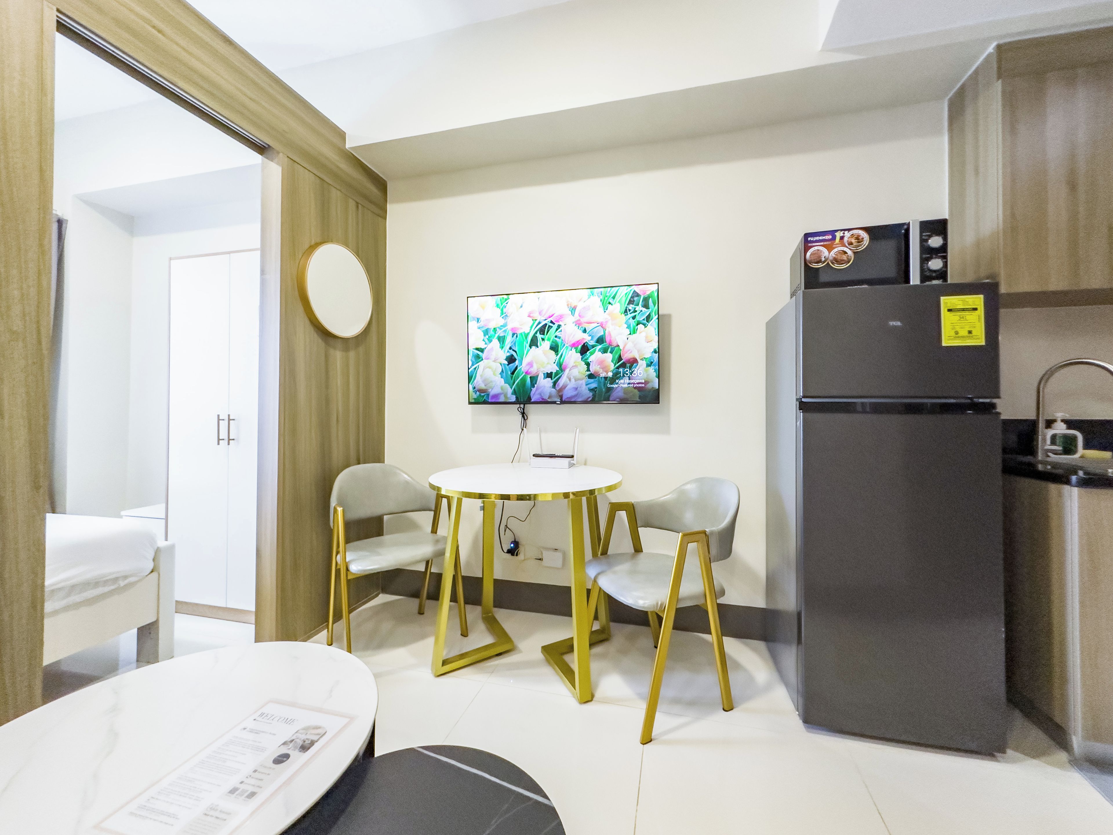 A modern kitchen with a refrigerator, a flat-screen TV, and a dining area with two chairs and a table.