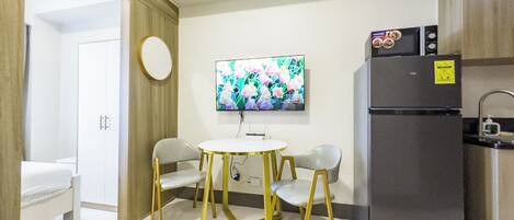 A modern kitchen with a refrigerator, a flat-screen TV, and a dining area with two chairs and a table.