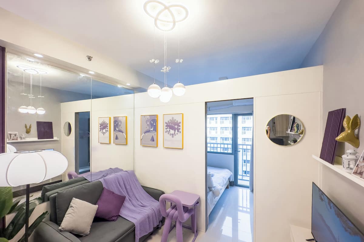 Un salon moderne avec un canapé, une petite table et un téléviseur. Les murs sont ornés de tableaux encadrés et il y a un miroir.