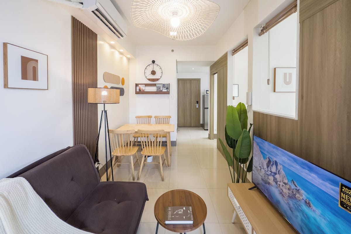 Un salon moderne comprenant un canapé, une table à manger avec des chaises, une lampe sur pied, un téléviseur et une grande plante.
