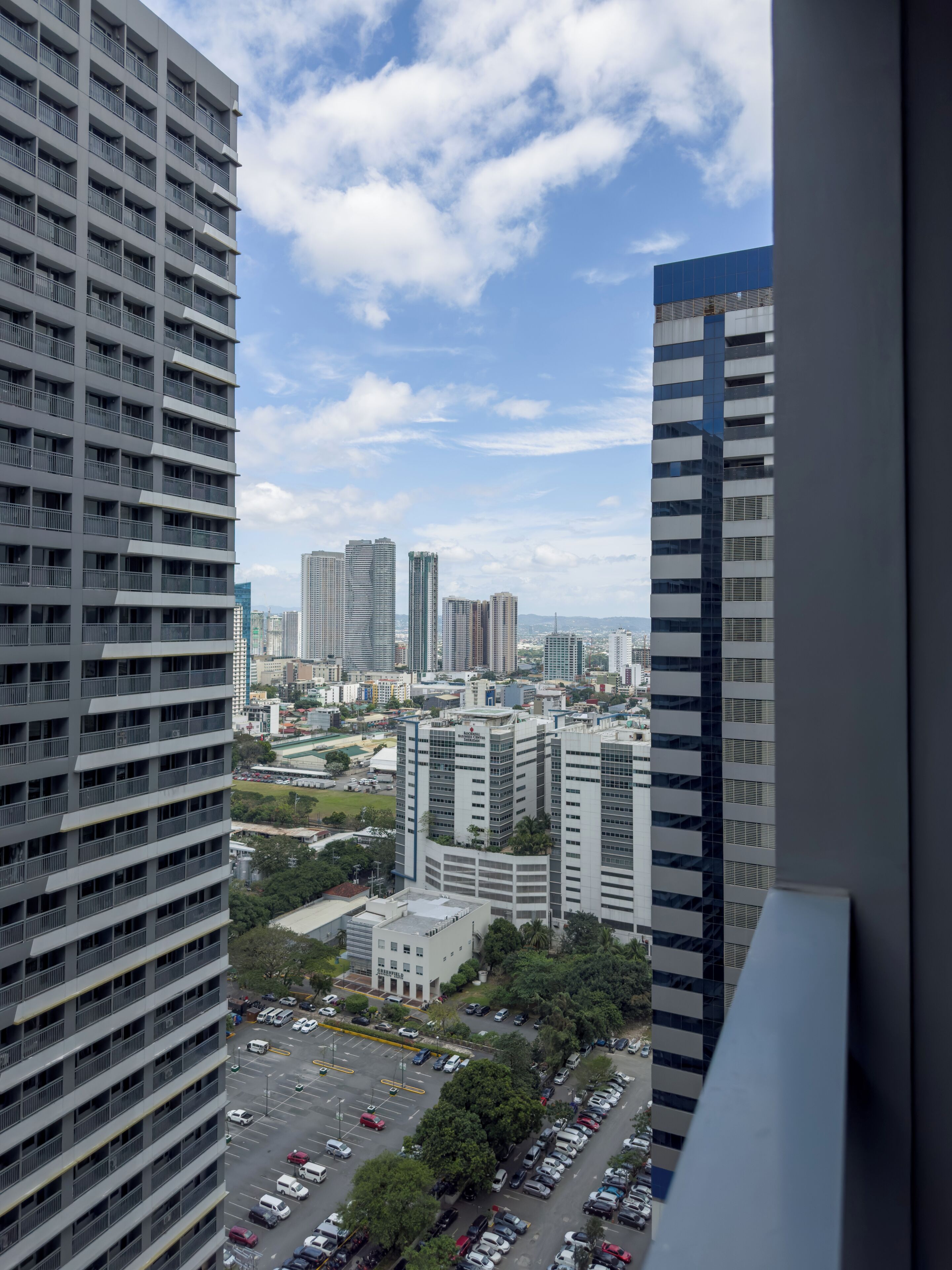 Un edificio de gran altura con varios pisos y balcones, rodeado de otros edificios altos y un estacionamiento en la parte inferior.