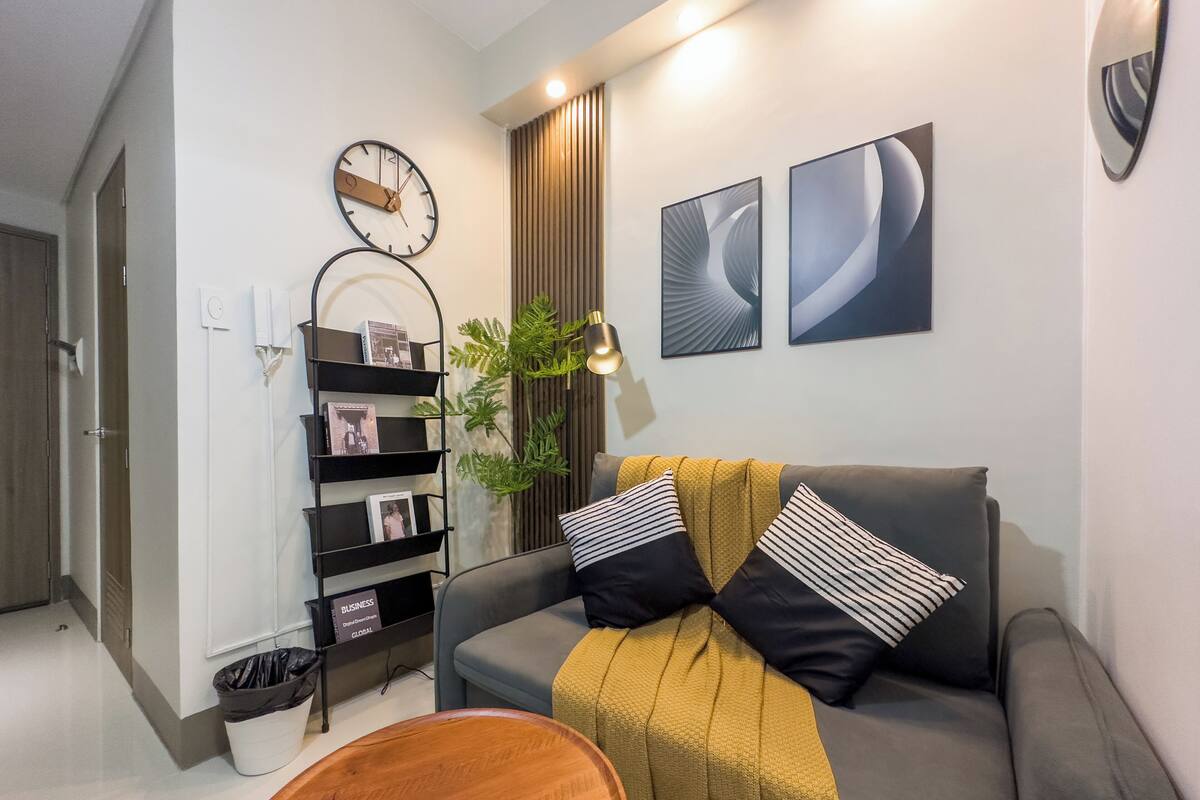 Un salon moderne avec un canapé gris, une table basse en bois, une bibliothèque noire et deux tableaux abstraits accrochés au mur.