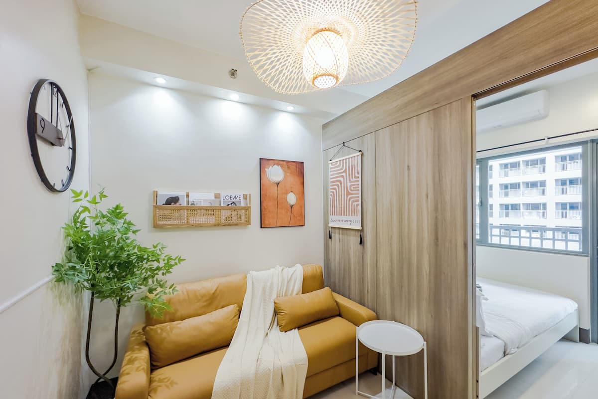 Une pièce moderne et bien éclairée, avec un canapé, une petite table, une plante en pot et un lit.