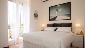 Un dormitorio con una cama grande, dos mesitas de noche con lámparas, un cuadro en la pared y una ventana con cortinas traslúcidas.