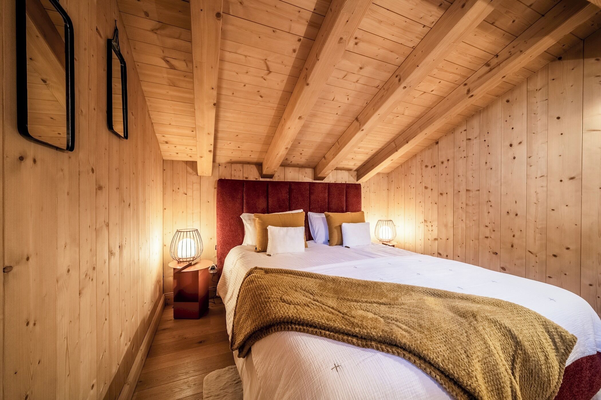 Quarto com painéis de madeira, cama, almofadas e abajures.