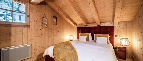 A wooden cabin bedroom with a large bed, a radiator, and a window with a view of the outdoors.