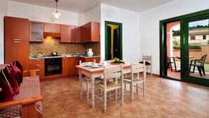 A compact kitchen with wooden cabinets, a dining table with chairs, and a view to the outside.