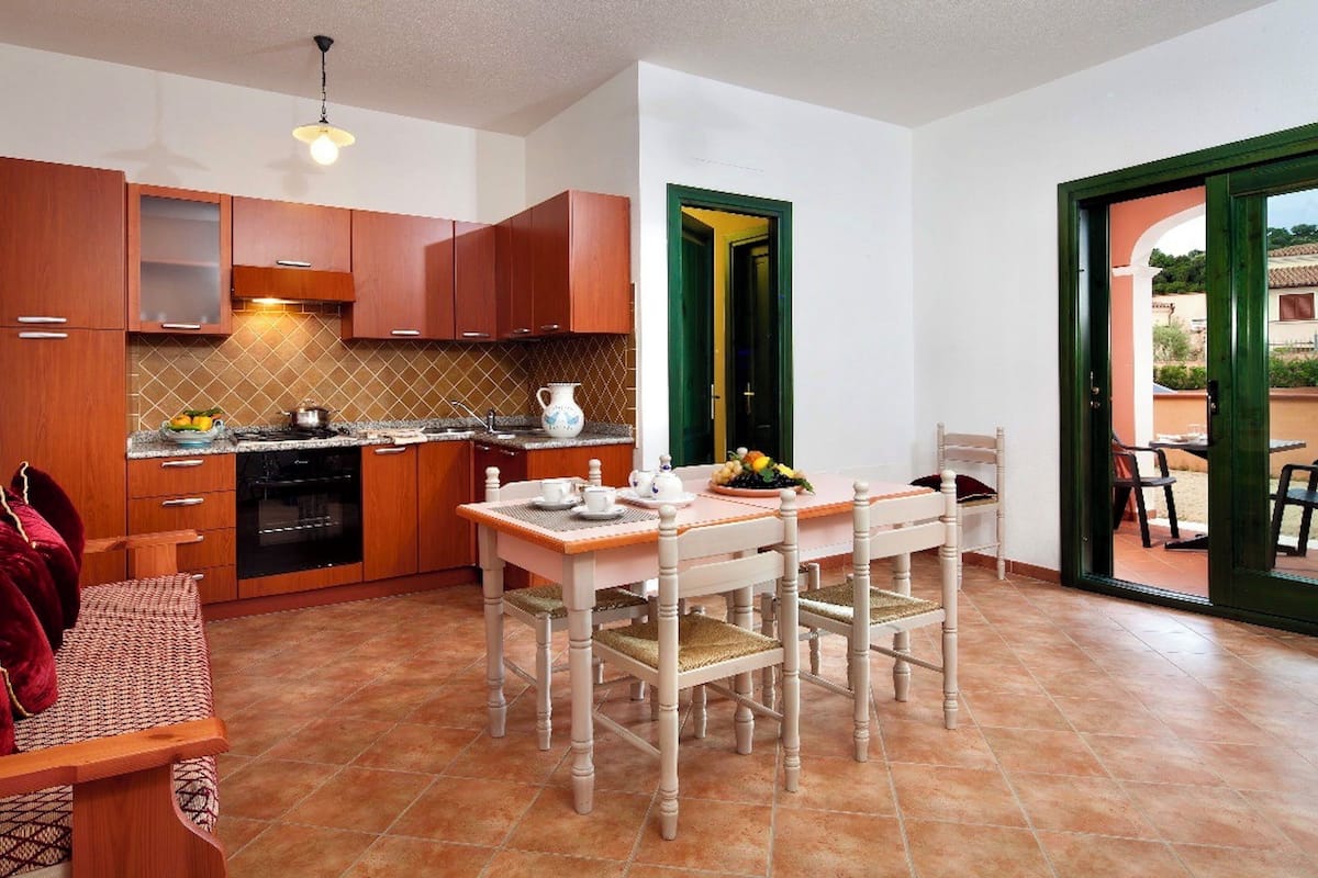 Una cucina compatta con mobili in legno, un tavolo da pranzo con sedie e vista all'esterno.