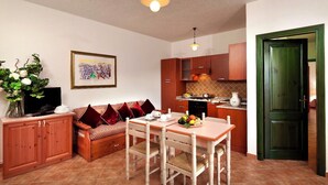A compact living space with a dining area, a sofa with cushions, a television on a cabinet, and a kitchen area with cabinets and a countertop.