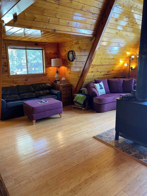 L’intérieur d’un chalet accueillant, avec un plafond en bois, un canapé, une causeuse, une table et une horloge.