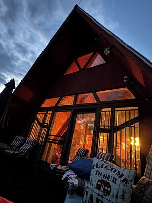Une cabane dotée d’une grande fenêtre à l’avant, d’un porche avec des chaises et d’une pancarte de bienvenue.