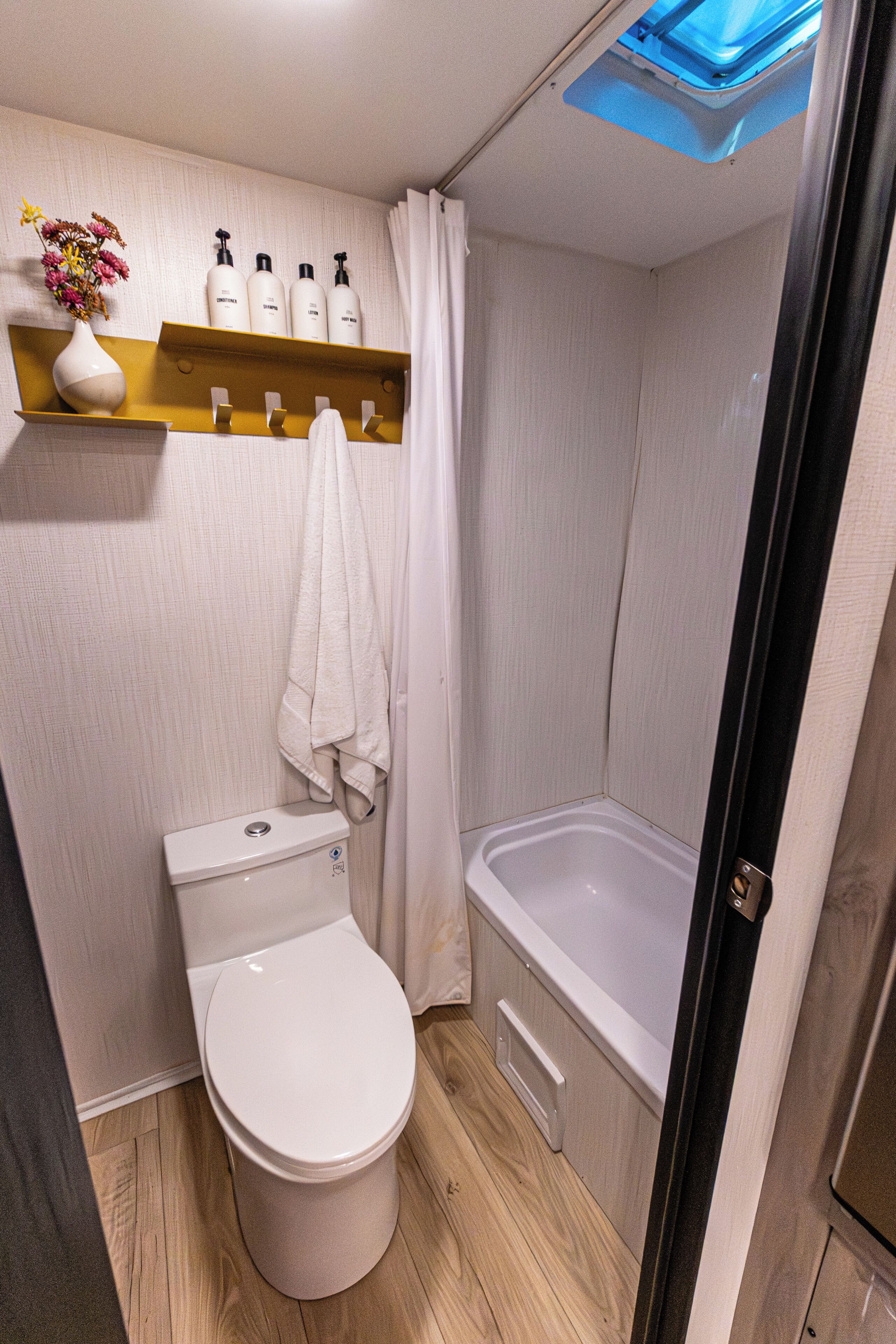 Un baño pequeño con inodoro, ducha y estante con artículos de aseo.