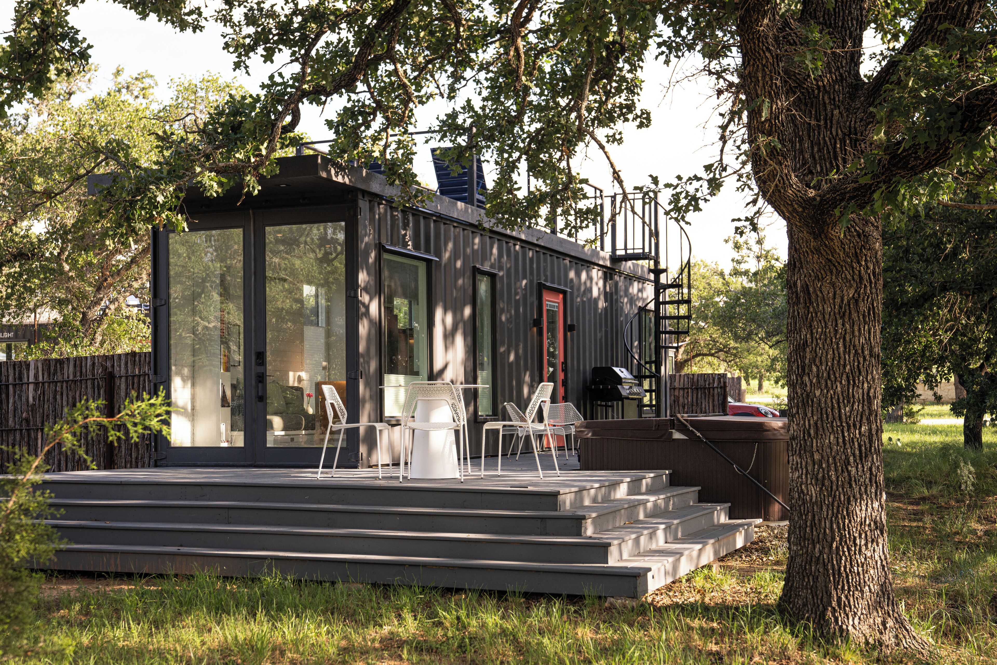 A modern house with a glass door, a red door, and a staircase leading to a deck with outdoor furniture.