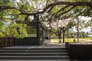 A wooden deck with steps leading to a glass-enclosed structure, surrounded by trees and a covered seating area.