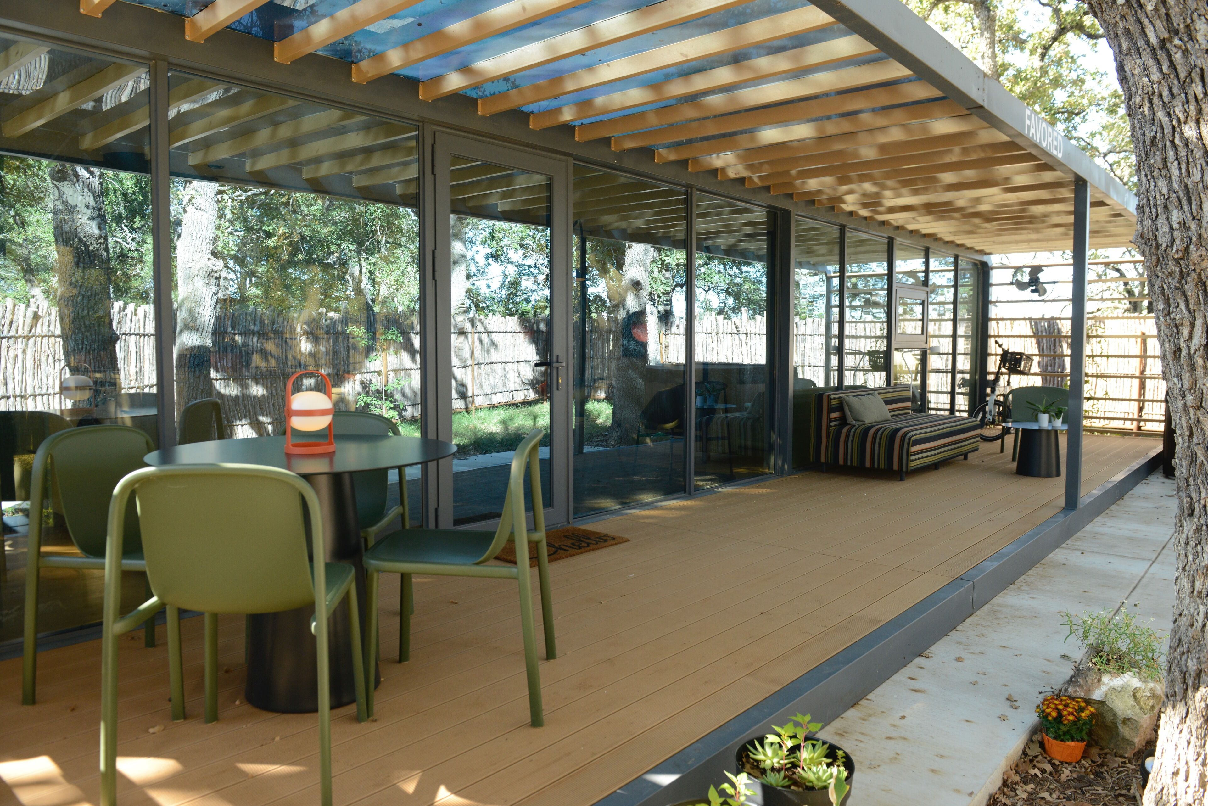 A covered patio with a glass enclosure, outdoor seating, and potted plants.