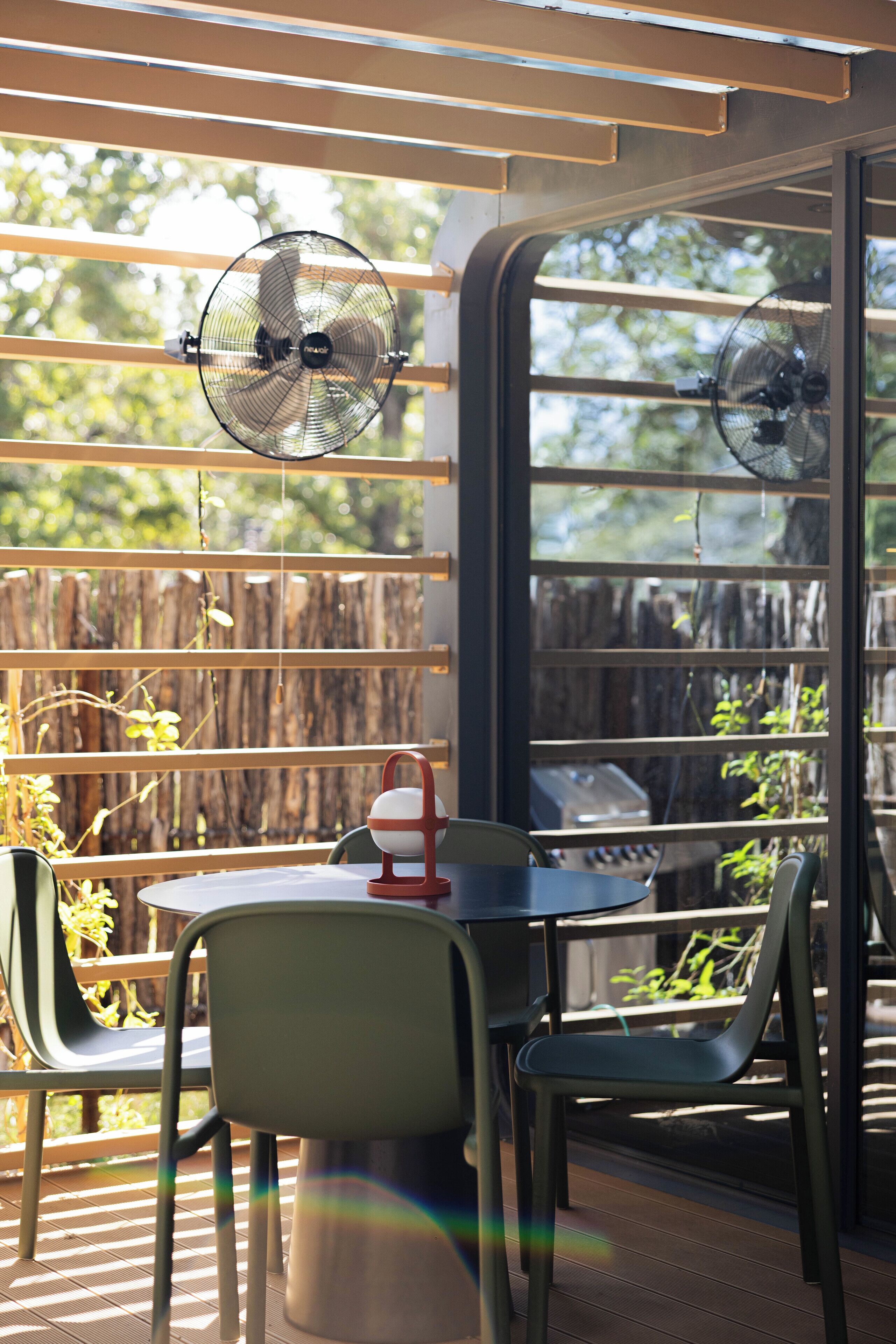 A patio area with a table and chairs, a fan, and a view through a window.